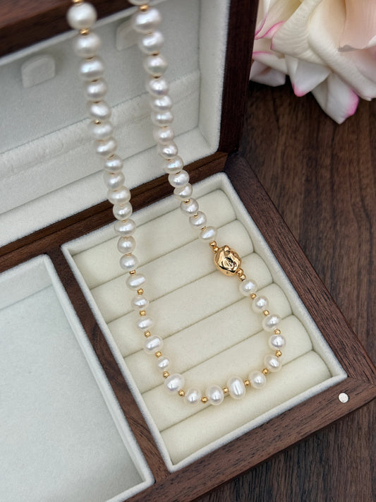 Natural pearl necklace in open jewelry box, gold-tone clasp visible, long bead strands