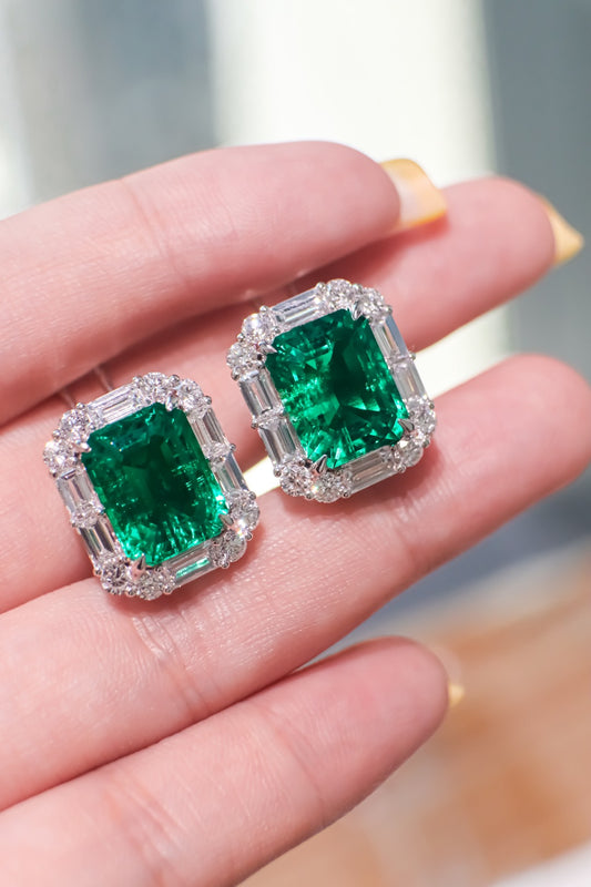Square emerald stud earrings with diamond halo and baguette accents, shown on fingers