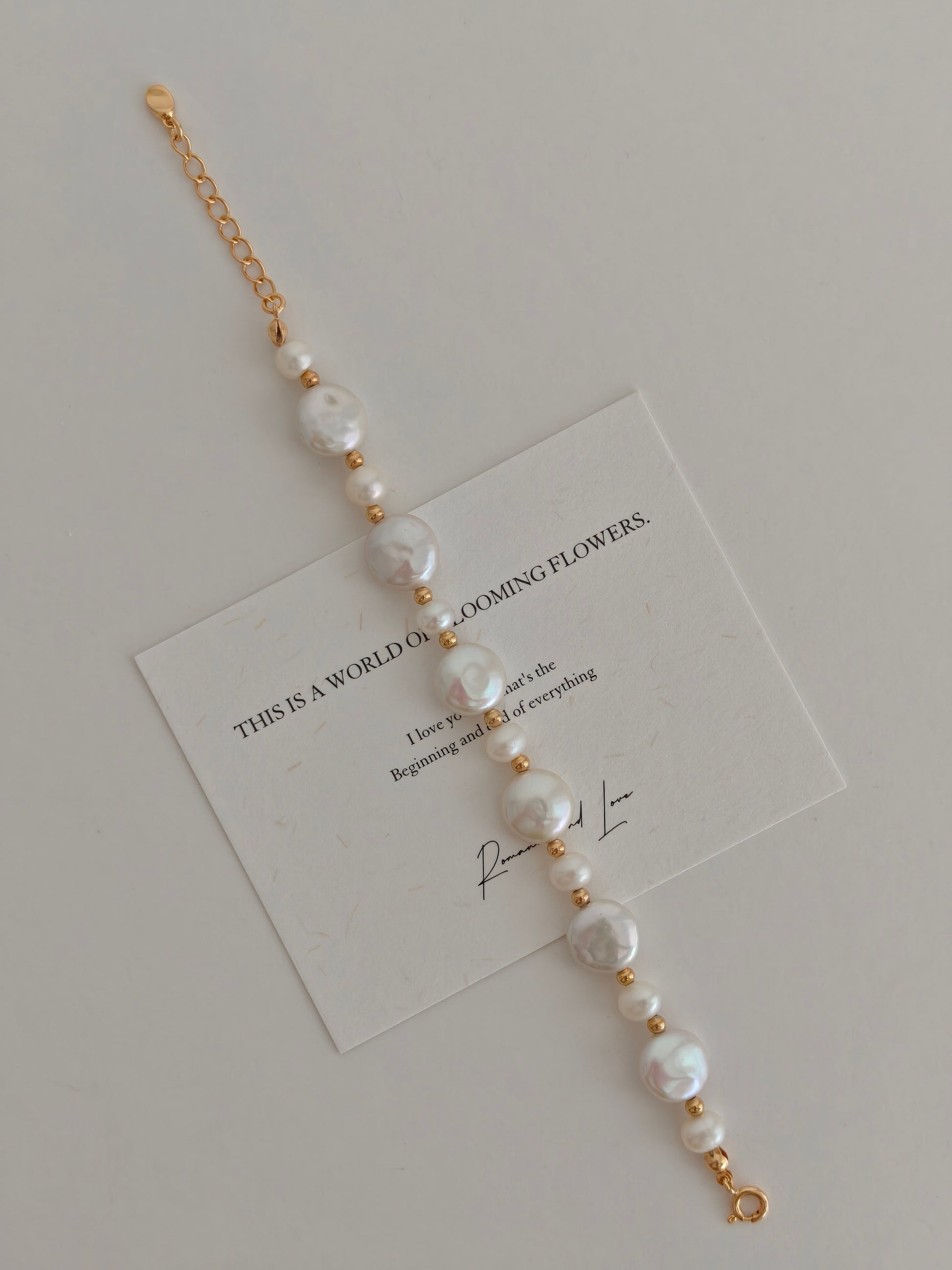 Pearl button bracelet with gold-tone chain and white pearls, laid on card