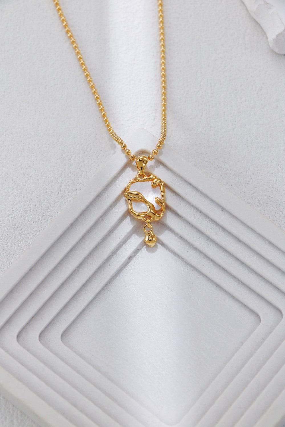 Gold-tone mother-of-pearl heart pendant necklace on textured display