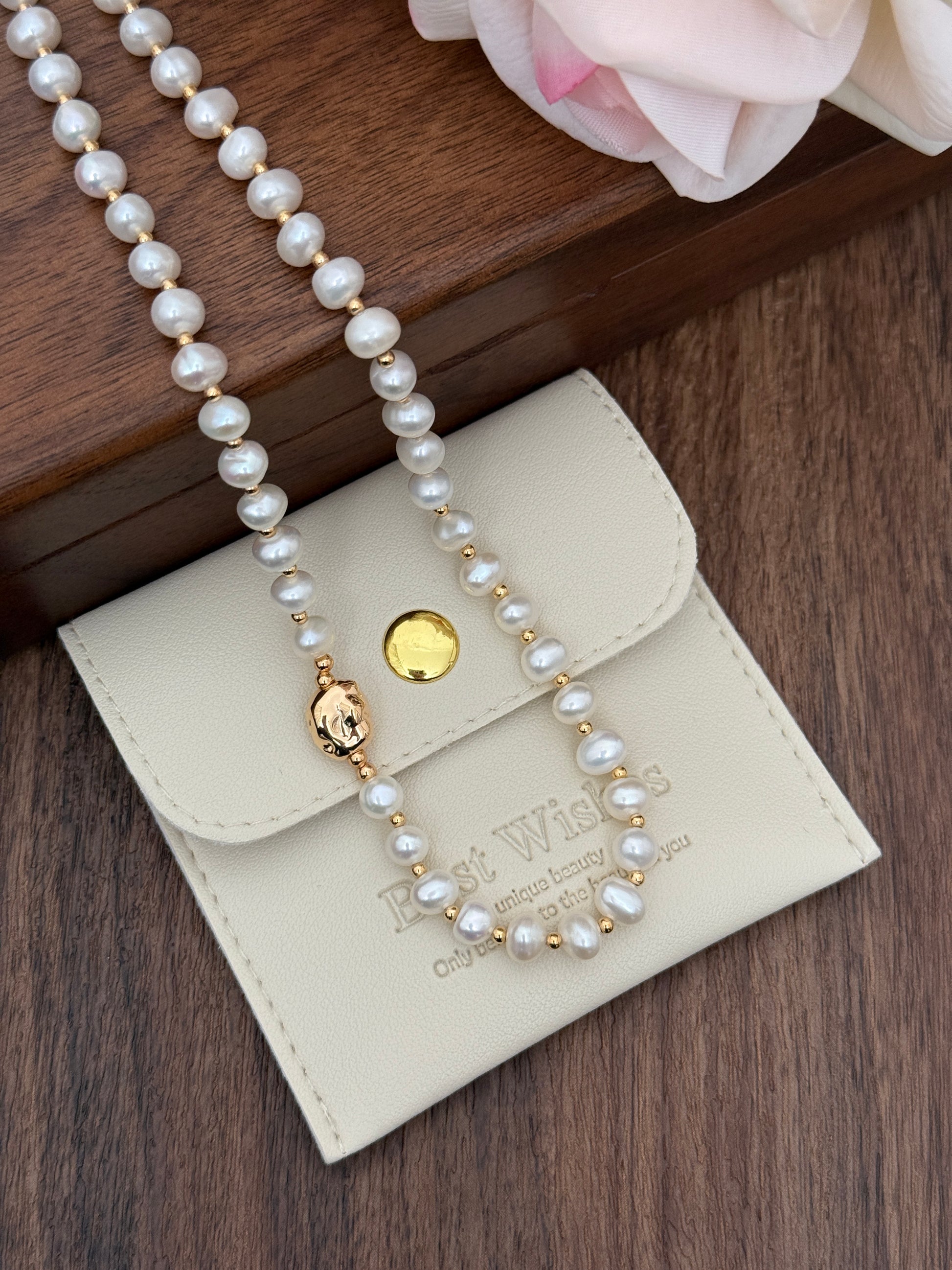 Natural pearl necklace close-up on cream case, gold-tone clasp with small dangling charm