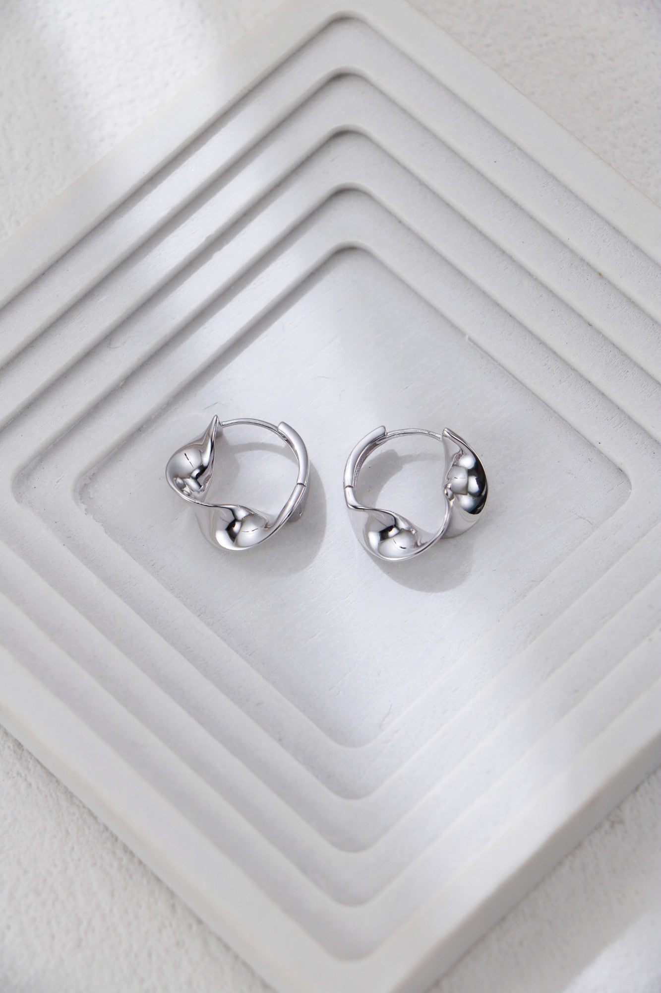 Twisted hoop earrings in silver on a jewelry tray, knot-like twist at front
