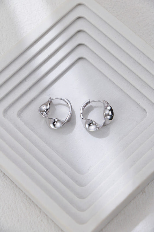 Twisted hoop earrings in silver on a jewelry tray, knot-like twist at front