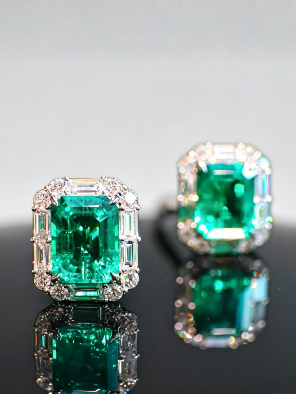 Pair of emerald stud earrings with square emerald centers and diamond halo, mirrored close view